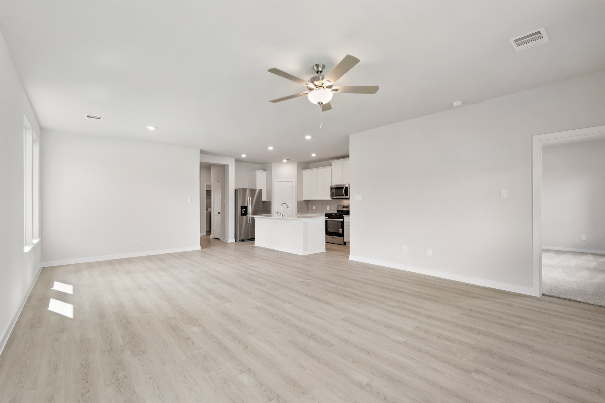 A large empty room with a ceiling fan and a wood floor.