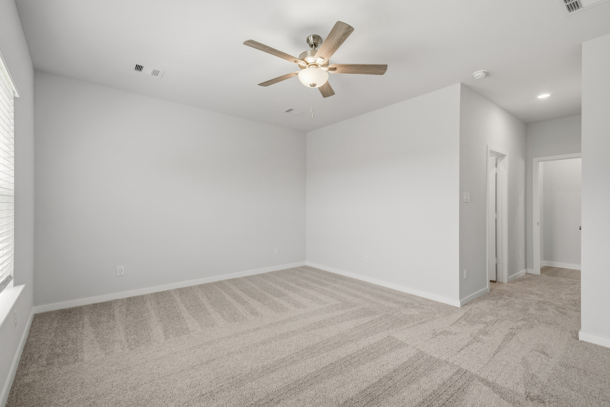 A room with a ceiling fan and a carpet.