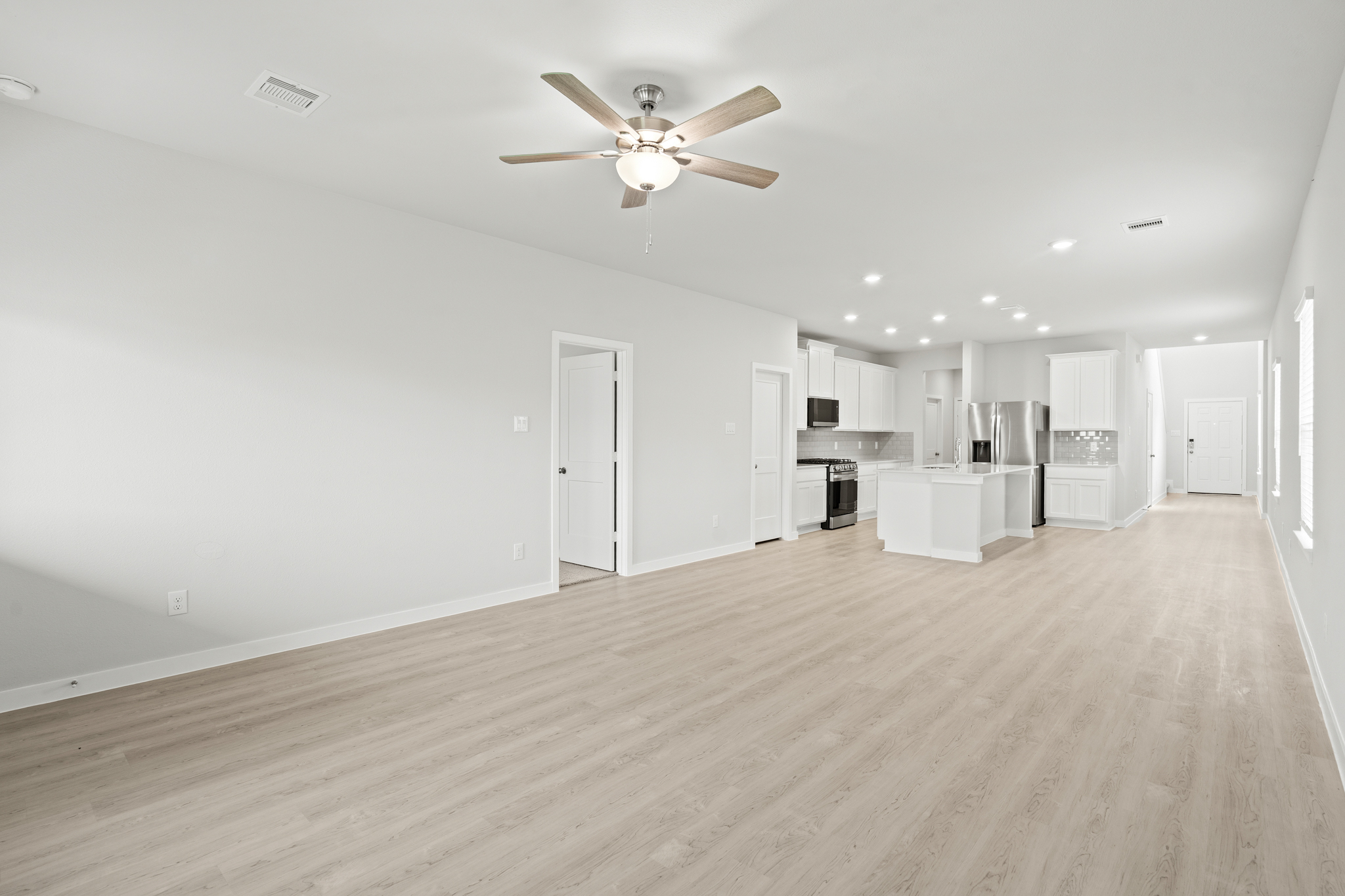 A large empty room with a ceiling fan and white cabinets.