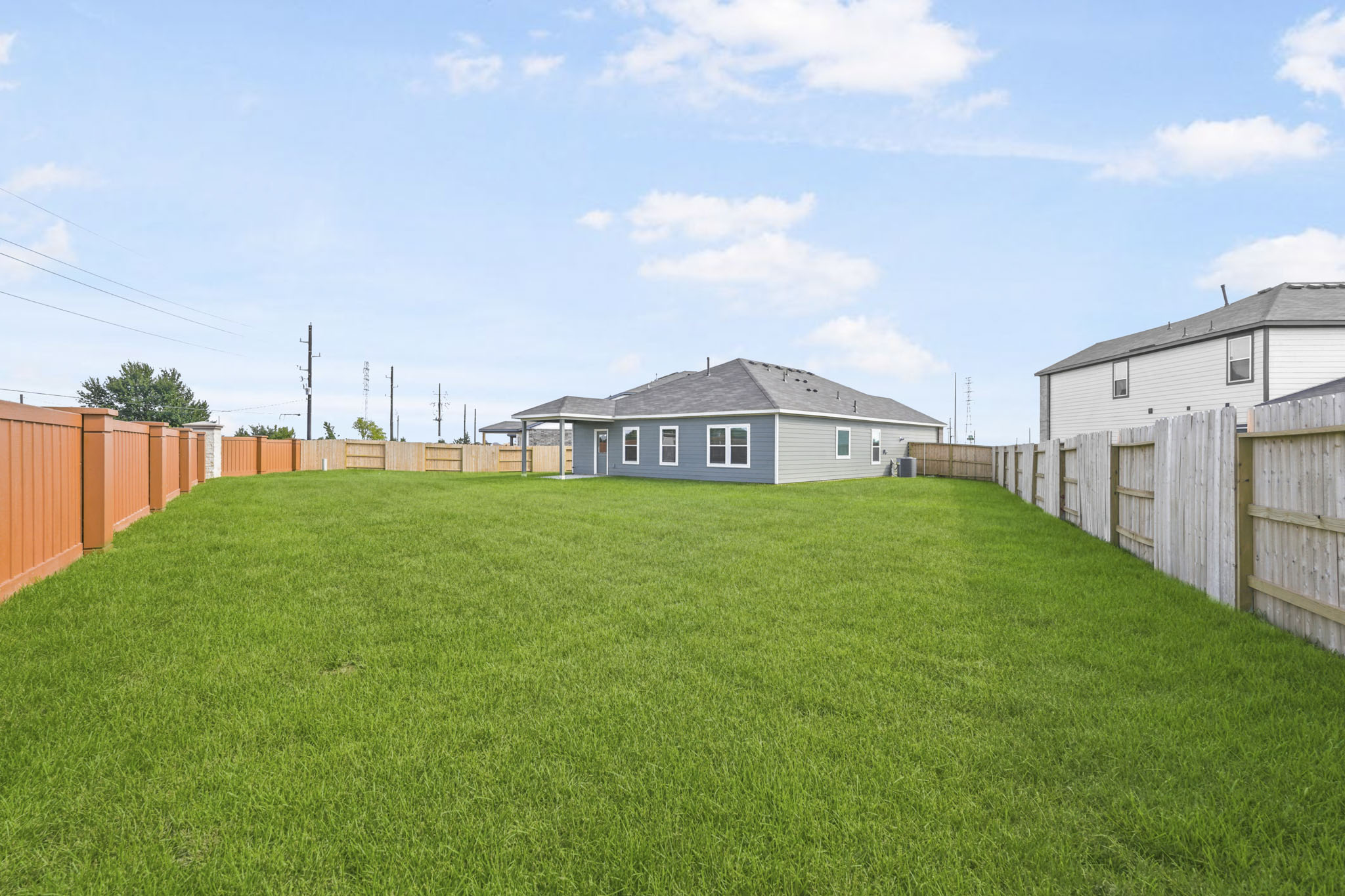 A grassy yard with a fence and a house in the background.