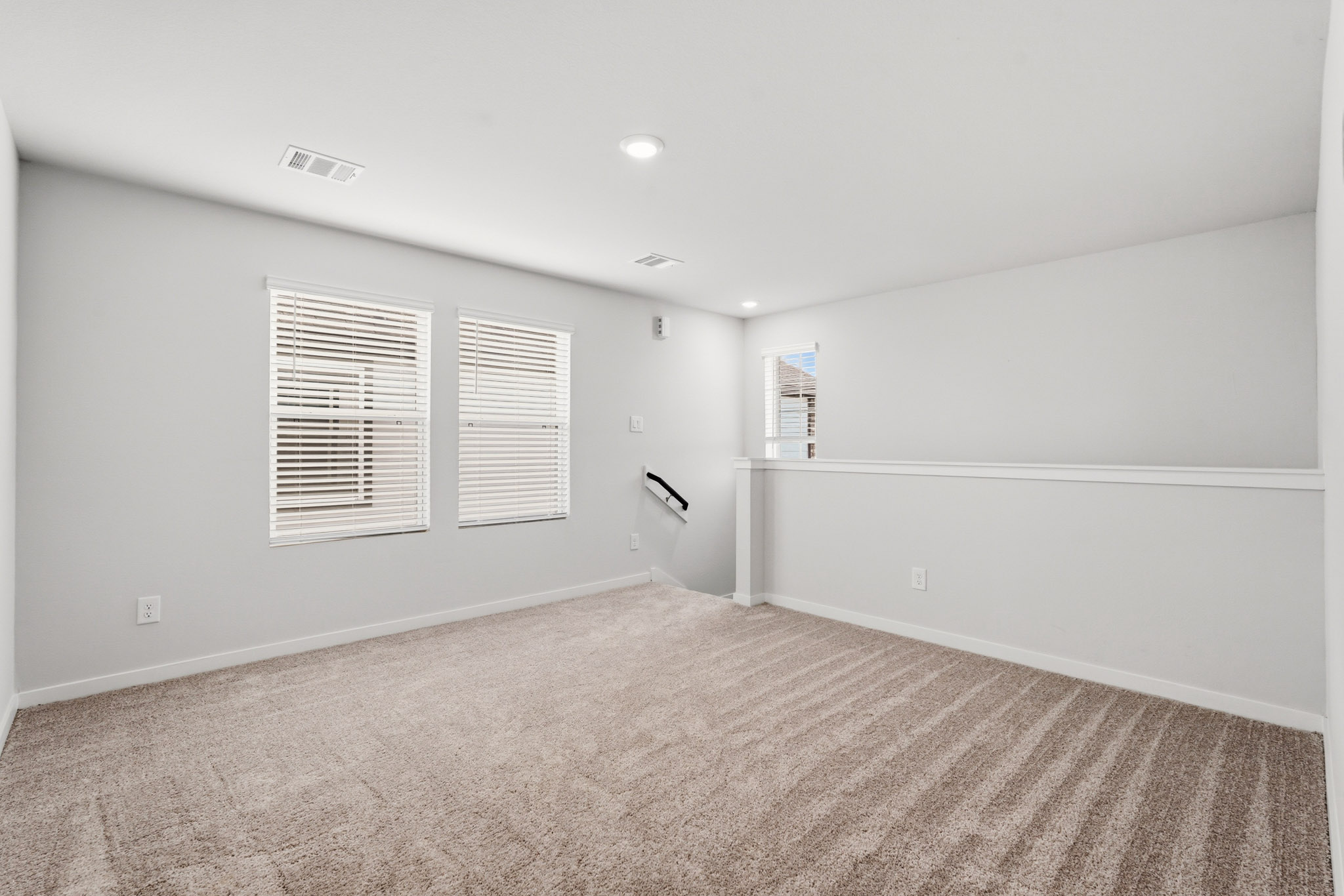 A room with a carpet and a white wall with a vent.