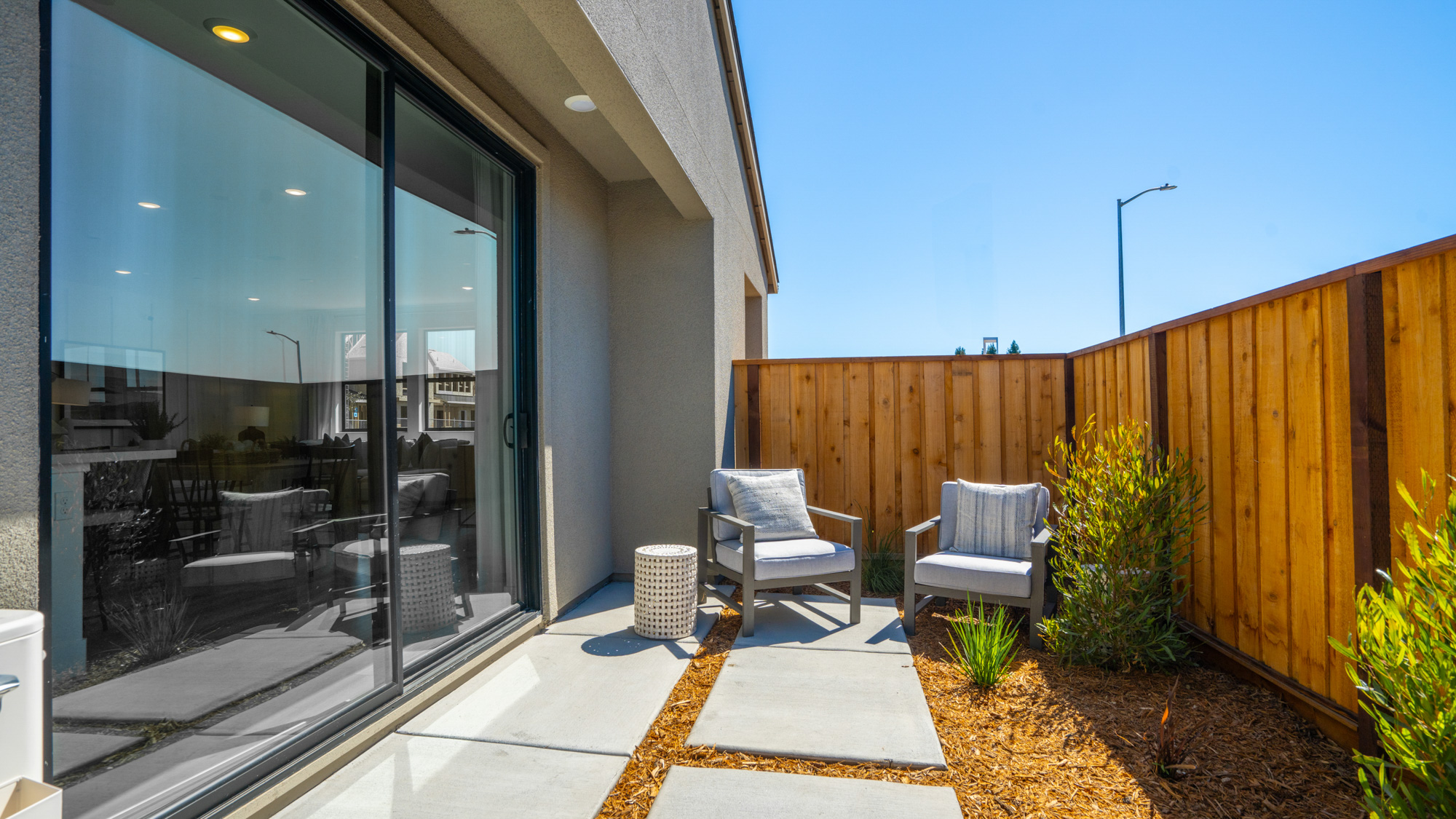 A patio with chairs and a glass door with a wood fence and a wood fence and a blue.